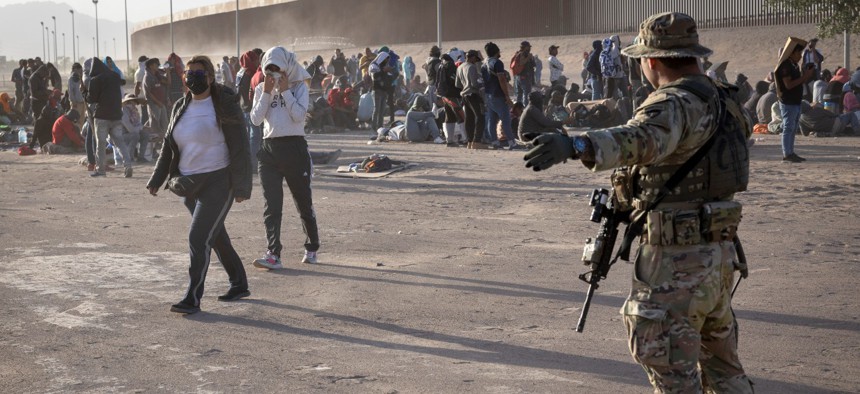 A Texas National Guard soldier directs immigrants during a dust storm at a makeshift camp located between the Rio Grande and the U.S.-Mexico border fence on May 10 in El Paso, Texas. The president is sending thousands of federal personnel to help at the border in response to a policy change expected to double the number of daily migrant encounters at the southwest border. 